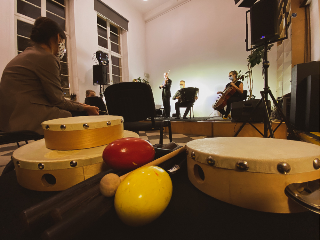 Na pierwszym planie znajdują się różne instrumenty muzyczne, na drugim - scena z muzykami.
