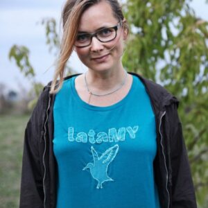Kamila Chomicz w niebieskiej koszulce z wyszytym na niej napisem lataMY i konturem ptaka w locie