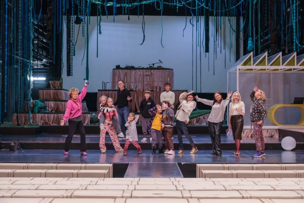 Uczestnicy oraz prowadzący stoją na scenie teatralnej i uśmiechają się do zdjęcia.