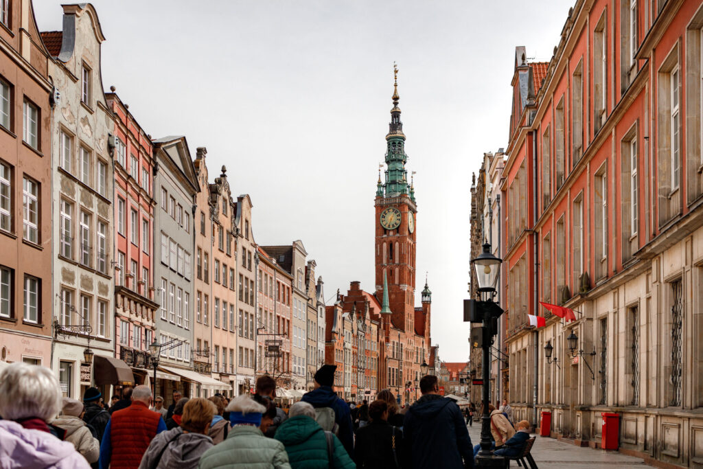 Grupa uczestników idzie między kamienicami w kierunku Kościoła Mariackiego.